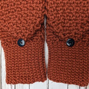 May include: Close-up of the cuffs of a rust-colored knitted sweater with two black buttons.