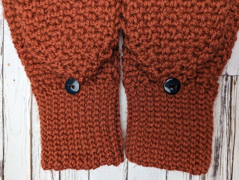May include: Close-up of the cuffs of a rust-colored knitted sweater with two black buttons.