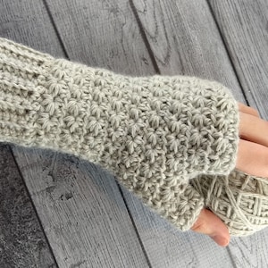 Op de afbeelding: Een paar beige gebreide vingerloze handschoenen met een textuurpatroon. De handschoenen worden getoond op een houten oppervlak.