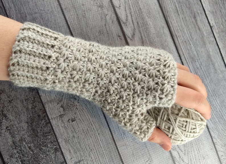 Op de afbeelding: Een paar beige gebreide vingerloze handschoenen met een textuurpatroon. De handschoenen worden getoond op een houten oppervlak.