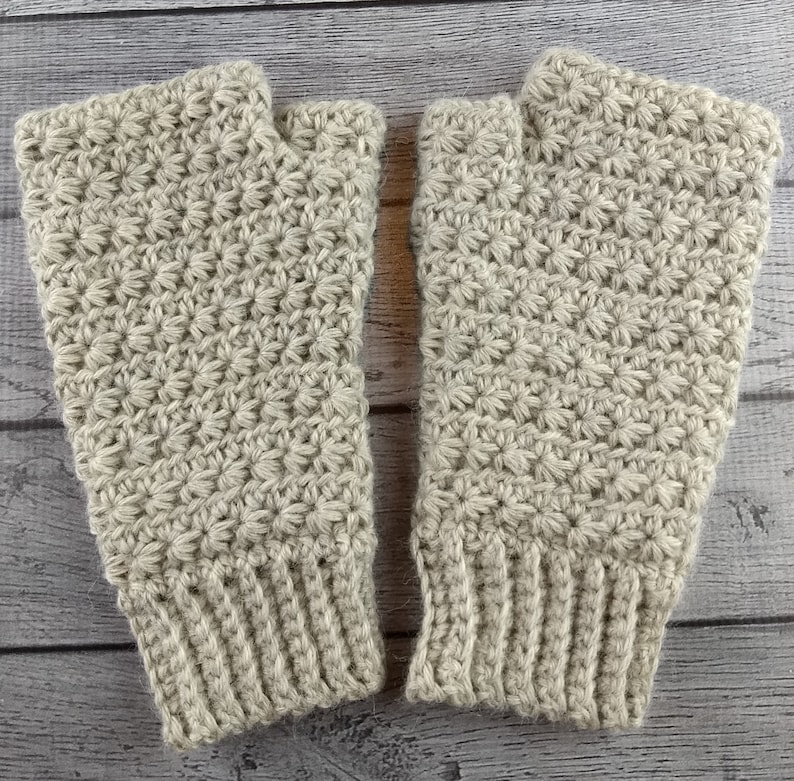 Op de afbeelding: Een paar beige gebreide vingerloze handschoenen met een sterrensteekpatroon.