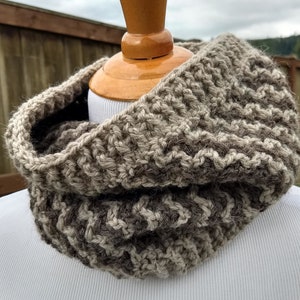 May include: A brown and beige crocheted cowl neck scarf. The scarf is made with a textured stitch pattern.