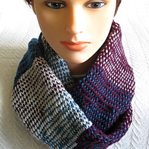 May include: A knitted infinity scarf with a striped pattern in shades of burgundy, teal, and gray.