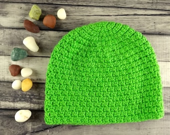May include: A bright green crocheted beanie hat. The hat is made with a simple stitch pattern and has a rounded crown.