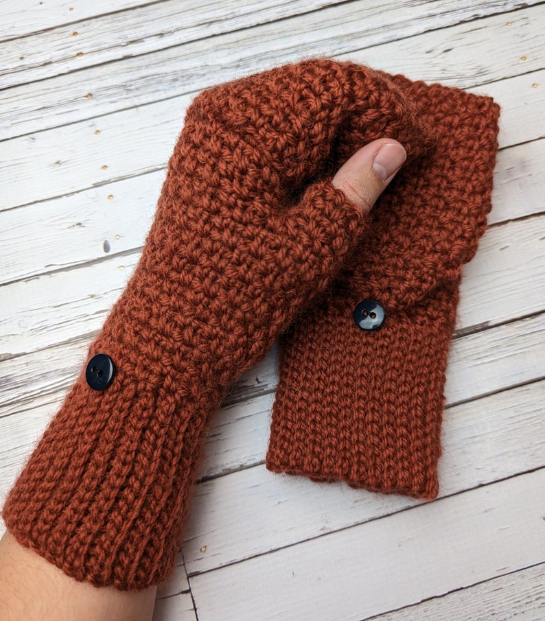 May include: A pair of brown crocheted fingerless gloves with black buttons. The gloves are made with a textured stitch and have a fold-over cuff.