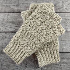 Op de afbeelding: Een paar beige gebreide vingerloze handschoenen met een textuur van sterrensteek.