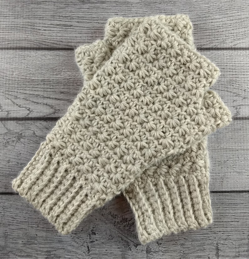 Op de afbeelding: Een paar beige gebreide vingerloze handschoenen met een textuur van sterrensteek.