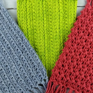 May include: Three crocheted macrame wall hangings in different colors: light blue, green, and red. Each hanging has a fringe at the bottom.