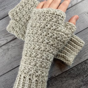 Op de afbeelding: Een paar beige gebreide vingerloze handschoenen met een textuurpatroon. De handschoenen worden getoond op een houten oppervlak.