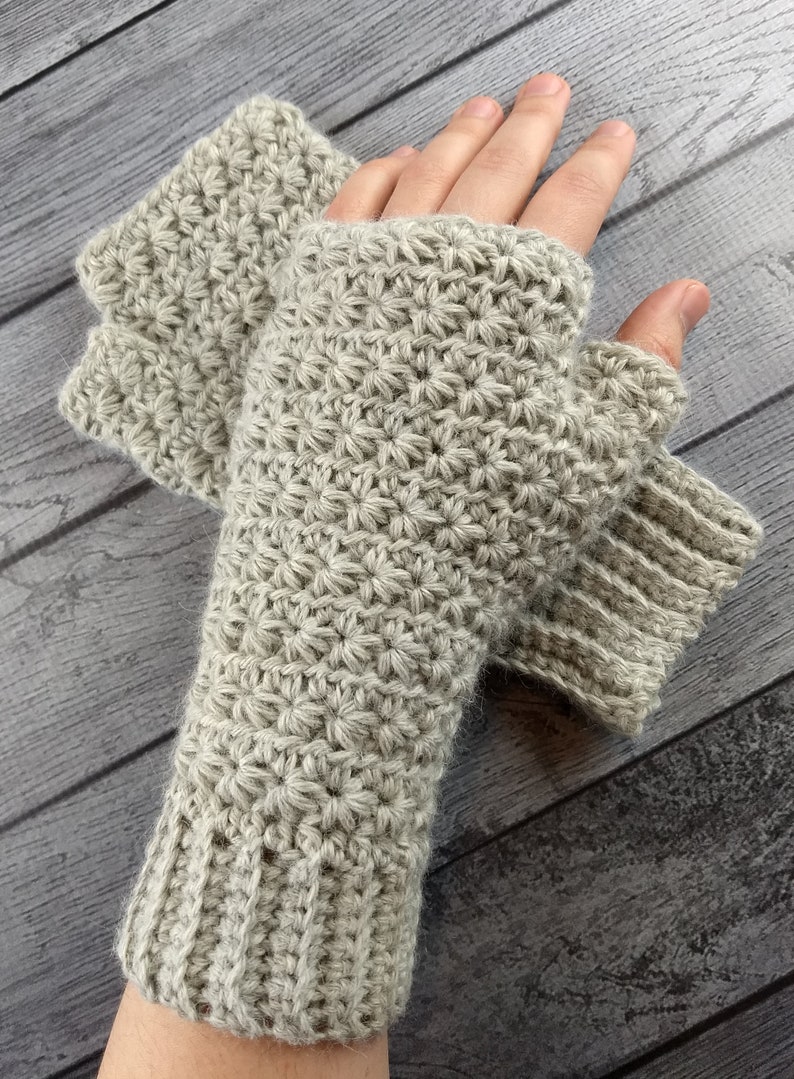 Op de afbeelding: Een paar beige gebreide vingerloze handschoenen met een textuurpatroon. De handschoenen worden getoond op een houten oppervlak.