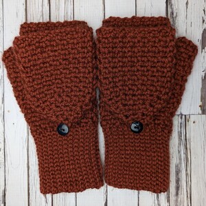 May include: A pair of brown crocheted fingerless gloves with black buttons. The gloves are made with a textured stitch and have a warm, cozy look.