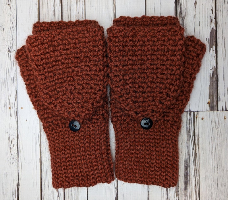 May include: A pair of brown crocheted fingerless gloves with black buttons. The gloves are made with a textured stitch and have a warm, cozy look.