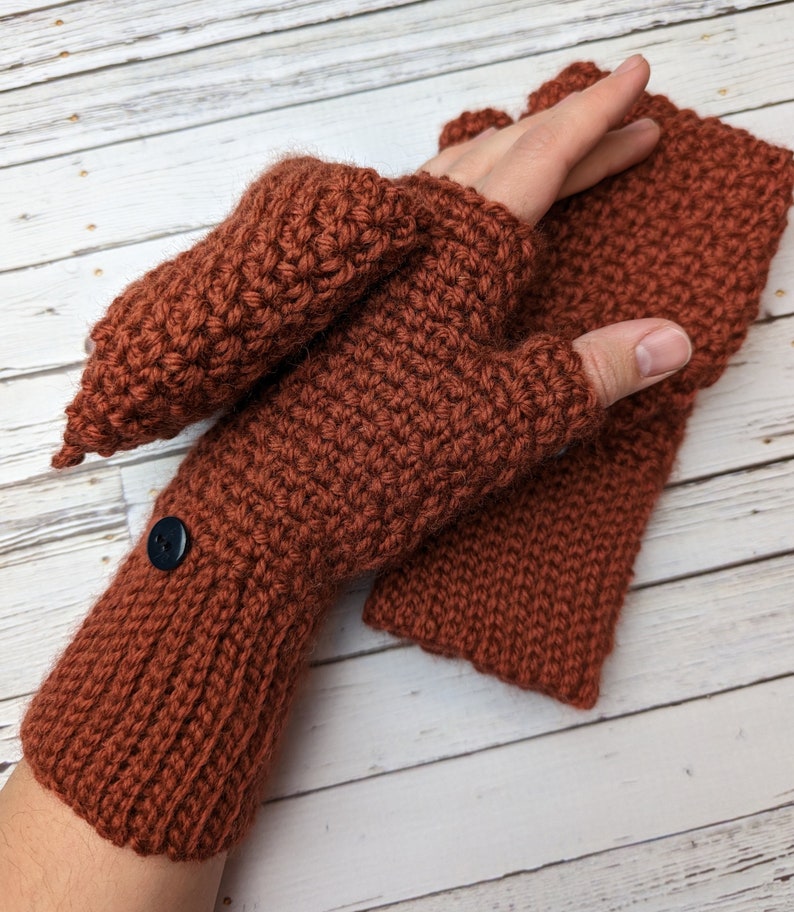 May include: A pair of brown crocheted fingerless gloves with a button on the wrist. The gloves are made with a textured stitch and have a fold-over cuff.