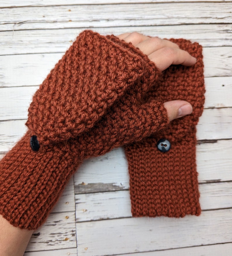 May include: A pair of brown knitted fingerless gloves with a button on the cuff. The gloves are made with a textured stitch.