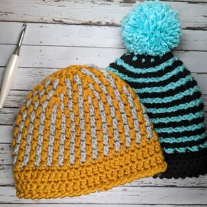 Peut inclure: Deux bonnets en crochet, l'un à rayures jaunes moutarde et grises et l'autre à rayures noires et turquoise avec un pompon turquoise.