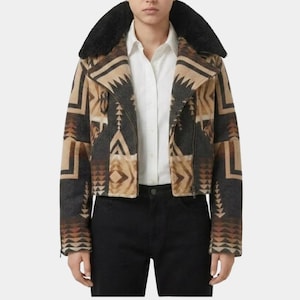 May include: A cropped jacket featuring a geometric pattern in shades of brown, tan, and charcoal gray. The jacket has a wide black faux fur collar, long sleeves, and a front zipper closure, worn over a white button-down shirt and black pants.