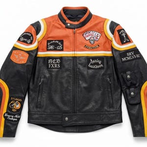 Könnte beinhalten: Eine schwarze Motorradjacke aus Leder mit orangefarbenen und gelben Rennstreifen an den Ärmeln und auf der Brust. Die Jacke ist mit verschiedenen gestickten Aufnähern verziert, darunter ein Totenkopf mit Spielkarten, Harley Davidson Schriftzug und Sturgis-Logos.