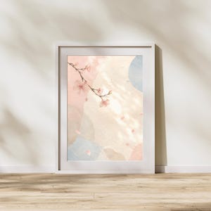 以下が含まれることがあります： 水彩デザインの額入りアートプリント。ピンクの桜の花と落ちる花びらの枝が、ソフトピンク、ブルー、ベージュの抽象的な形の背景に描かれています。プリントは白いフレームに表示されています。