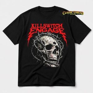 Può includere: Una t-shirt nera a maniche corte con la grafica di un teschio umano circondato da filo spinato. Sopra il teschio, il testo recita KILLSWITCH ENGAGE in un carattere rosso frastagliato. Il logo Classic Thread Apparel è stampato in alto a destra.