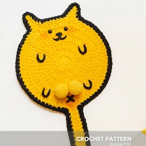 Può includere: Un sottobicchiere giallo all'uncinetto a forma di gatto con contorni e dettagli neri. Il sottobicchiere presenta un volto sorridente, due piccoli pompon e il testo "CROCHET PATTERN" e "Digital PDF".