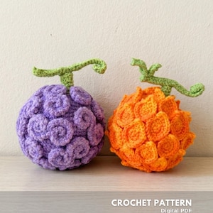 Può includere: Due frutti all'uncinetto. Uno è viola, l'altro arancione. Entrambi hanno steli verdi. Il frutto viola ha un motivo a spirale, mentre quello arancione ha un design segmentato. Il testo "CROCHET PATTERN" è visibile.