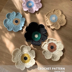 Può includere: Sei sottobicchieri a forma di fiore all'uncinetto fatti a mano in vari colori: azzurro, lavanda, beige, nero e bianco. Ogni sottobicchiere ha un centro a contrasto. Il testo "CROCHET PATTERN" e "CREATED BY @EMBRILLY" è visibile.