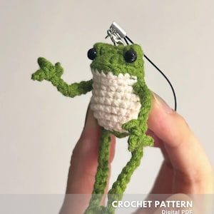 Può includere: Un piccolo oggetto a forma di rana all'uncinetto, verde e crema, con occhi neri. La rana è raffigurata con le braccia e le gambe tese. L'immagine include il testo "CROCHET PATTERN Digital PDF CREATED BY @EMBRILLY".