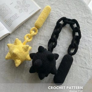 May include: Two crocheted maces, one yellow and one black, with spiked heads and cylindrical handles. The yellow mace has a chain link connecting the head and handle. The black mace has a chain link connecting the head and handle. A book with crochet patterns is in the background.