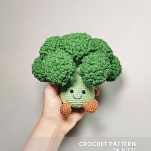 Può includere: Un peluche di broccoli all'uncinetto con un viso sorridente e piccoli piedi marroni. La testa del broccolo è verde strutturata e il gambo è verde chiaro. Il testo "CROCHET PATTERN" e "Digital PDF" è visibile.