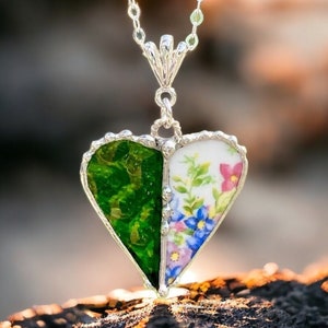 Puede incluir: Un collar de cadena de plata con un colgante en forma de corazón hecho de dos piezas de porcelana vintage. Un lado del corazón es verde con un patrón floral, y el otro lado es blanco con flores rosas y azules.