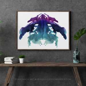 May include: A framed print of a symmetrical abstract watercolour design in shades of blue, purple, and green. The design resembles a Rorschach inkblot test. The text "Rorschach Art © DIMENSIONSOFWONDER.COM" is printed below the image.