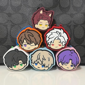 May include: A collection of six rubberized character charms featuring stylized anime-style heads with distinct hair colors including maroon, brown, white, black, blonde, and purple, each attached to a small colored ball chain loop.