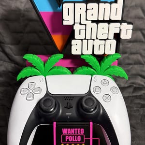 May include: A black and pink gaming controller stand featuring a large Grand Theft Auto VI logo with blue, pink, and orange accents. Two green palm trees sit behind the white and black controller. A sign reads WANTED POLLO with five stars.
