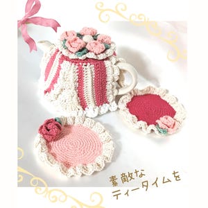 May include: A crocheted tea set featuring a teapot with a pink and white striped design, a lid with pink flower accents, and two matching coasters. The set includes the Japanese text "Enjoy a wonderful tea time."