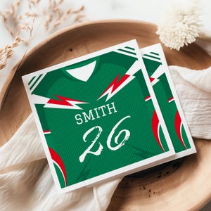 May include: Two square cards featuring a green sports jersey graphic with white accents, red lightning bolt details, and the text SMITH 26 printed in white. The design mimics a jersey with a V-neck collar and a textured mesh pattern on the fabric.