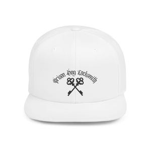 Op de afbeelding: Een witte baseballcap met een platte klep. De cap heeft de tekst "prison dog locksmith" in een gotisch lettertype, samen met een gekruist sleutelontwerp in zwart.