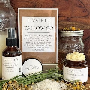 May include: A collection of Livvie Lu Tallow Co products including a brown glass spray bottle labeled Sweet Dreams Magnesium Spray, a small round tin, and a brown glass jar of Sweet Dreams Sleep Butter, accompanied by dried chamomile and salt.