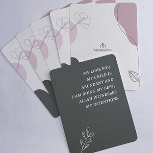May include: A collection of affirmation cards featuring a floral design and the text "Mamasbliss." The cards have a white background with pink accents and a grey card with the text "MY LOVE FOR MY CHILD IS ABUNDANT AND I AM DOING MY BEST, ALLAH WITNESSES MY INTENTIONS."