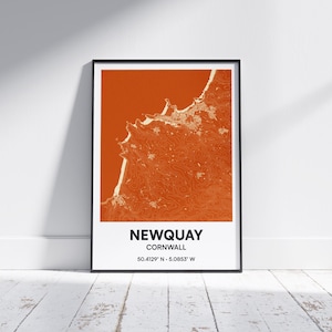 May include: Framed print featuring a topographic map of Newquay, Cornwall, in shades of orange and white. The town's name and coordinates are printed in black at the bottom. The print is displayed in a black frame against a white wall.