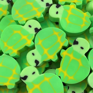 May include: A collection of green turtle-shaped erasers. Each eraser has a yellow pattern on its back and black details for the eyes and head. The erasers are scattered, creating a playful and colorful assortment.