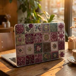 May include: A laptop computer featuring a protective hard shell case decorated with a grid of square tiles in shades of deep red, muted green, and cream. Each tile displays a unique, intricate floral or geometric pattern across the entire surface.