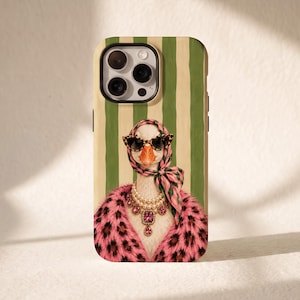 May include: A smartphone case featuring a graphic illustration of a goose wearing a pink leopard print coat, a pink patterned headscarf, cat-eye sunglasses, and a multi-layered pearl and pink gemstone necklace against a green and cream striped background.