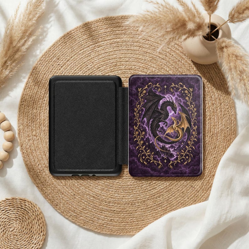 May include: A black e-reader case with a front cover featuring a dark purple stormy sky background, a large black dragon, and a smaller gold dragon intertwined within an ornate gold filigree frame of vines and leaves.
