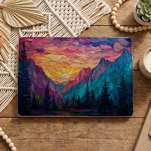 May include: A laptop case featuring a vibrant, stained-glass style mountain landscape with a sunset. The design showcases a colorful sky with shades of orange, pink, and purple, and the mountains are in shades of blue and green. The case is rectangular.