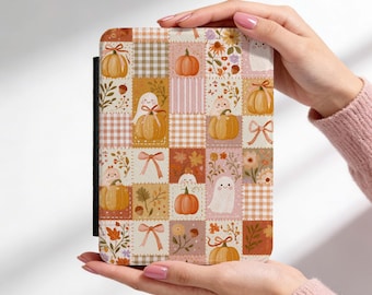 May include: A rectangular e-reader cover featuring a patchwork pattern of autumn-themed illustrations. The design includes orange pumpkins, white ghosts, pink bows, brown acorns, and various floral elements set against checkered and solid backgrounds.