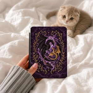 May include: A rectangular e-reader case featuring a dark purple, cloudy background with a large black dragon and a smaller gold dragon intertwined in the center. The design is framed by a decorative gold vine border with small rose-like details.