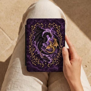 May include: A rectangular e-reader case featuring a dark purple background with swirling clouds and lightning. A large black dragon and a smaller gold dragon are depicted in the center, surrounded by an ornate gold vine frame with small flowers.