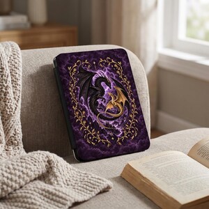 May include: A rectangular e-reader case featuring a dark purple cloudy background with lightning bolts. A large black dragon and a smaller gold dragon are intertwined in the center, surrounded by a decorative gold vine border with small leaves.
