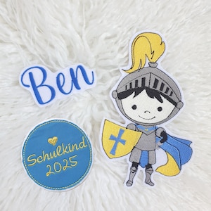 Könnte beinhalten: Gestickte Aufnäher mit einem Ritter, dem Namen "Ben" in blauer Schrift und einem blauen Kreis mit "Schulkind 2025" in Gold. Der Ritter hat eine gelbe Feder, einen Schild mit Kreuz und einen blauen Umhang.