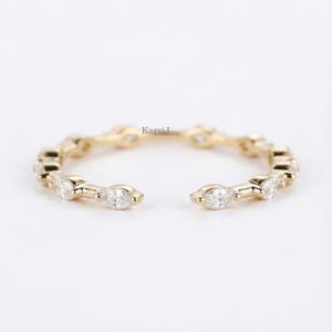 May include: A gold-toned open ring featuring a series of marquise-cut gemstones. The ring has a delicate design with the gemstones set in a repeating pattern. The ring is displayed on a white background.